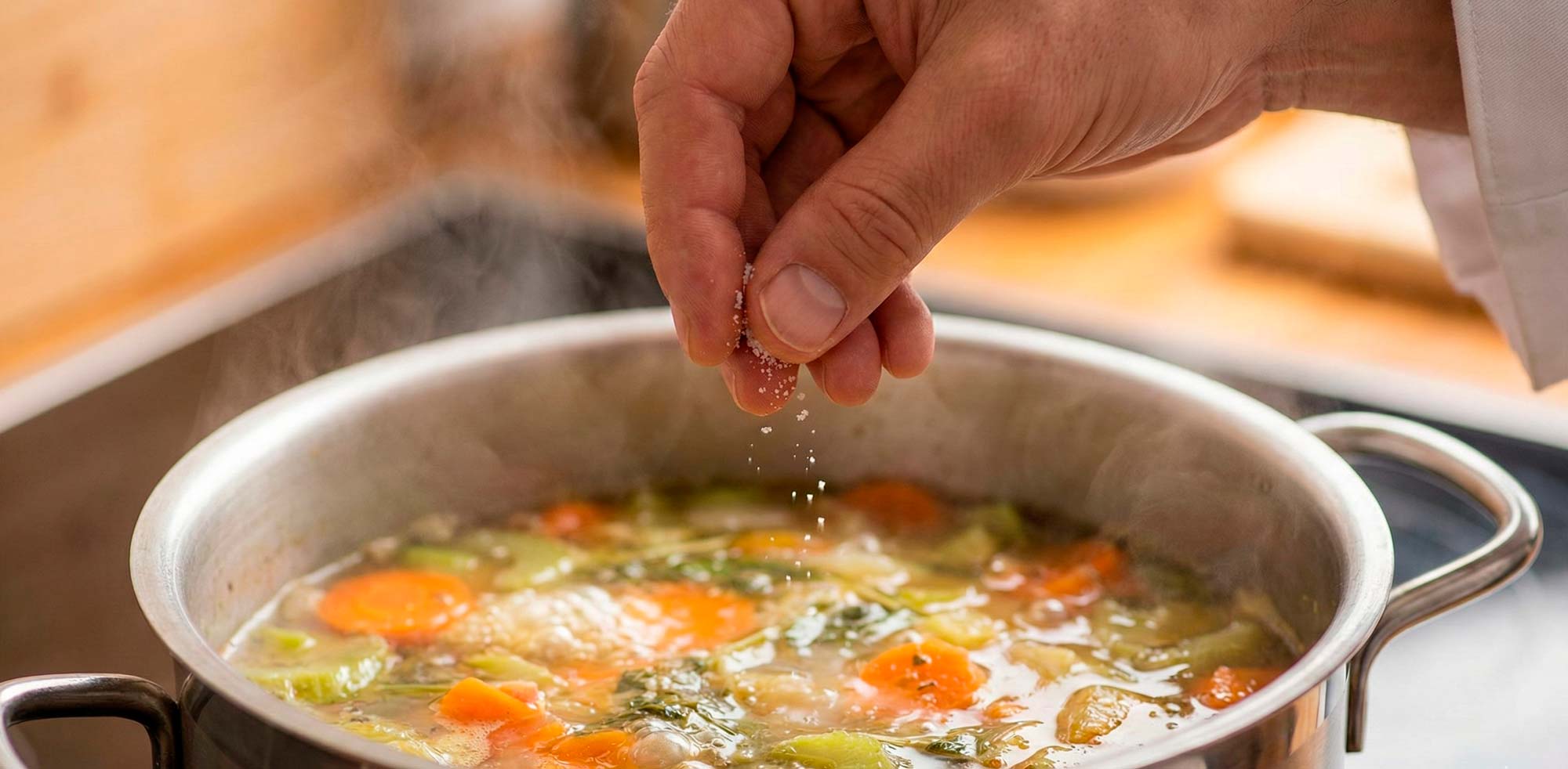 Close-up of a chef’s hand sprinkling a pinch of white seasoning.